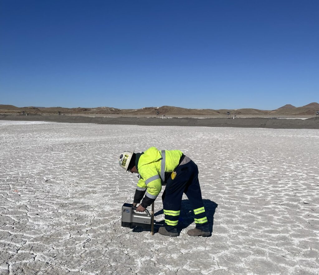 Worker in safety gear operating equipment on a dry, cracked surface at a coal ash remediation site, under a clear blue sky, emphasizing innovative approaches to coal combustion residual management.