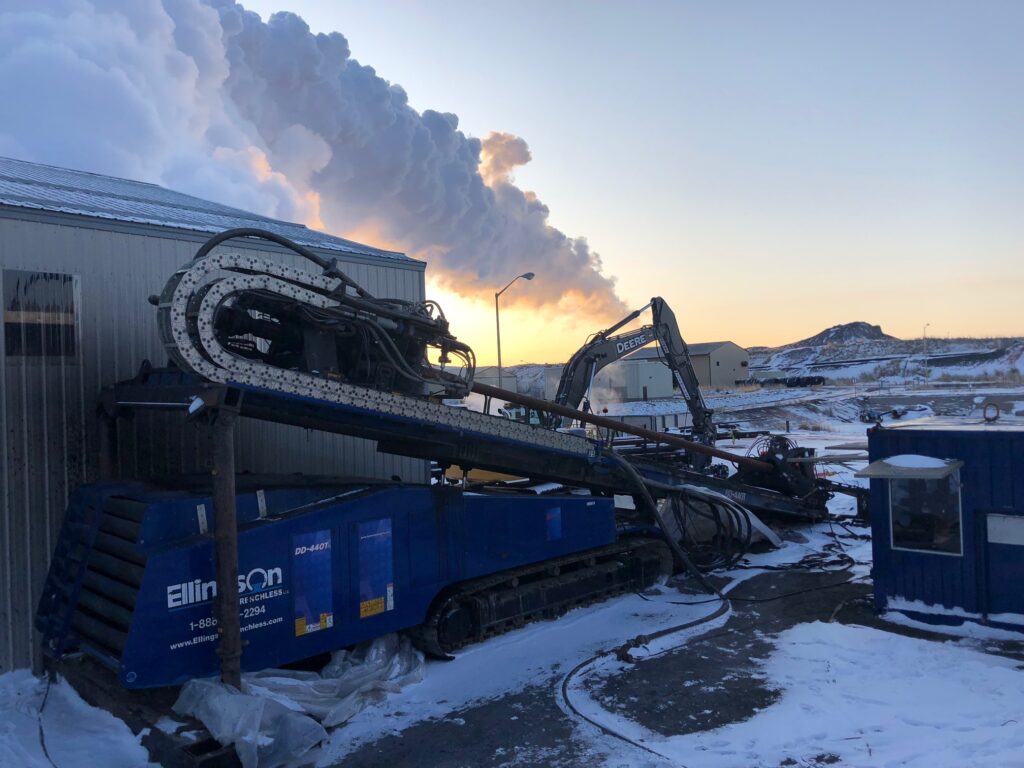 Horizontal drilling equipment at Ellingson Companies site for coal ash dewatering, with smoke in the background and snowy terrain.