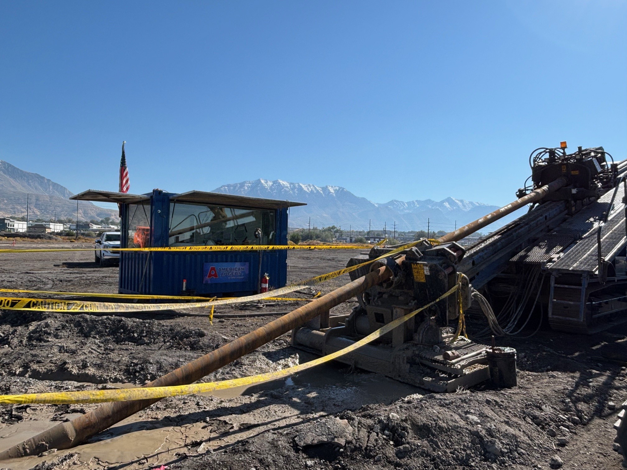 Construction site for coal ash dewatering, featuring horizontal drilling equipment, safety barriers, and a control container with an American flag, set against a mountainous backdrop.